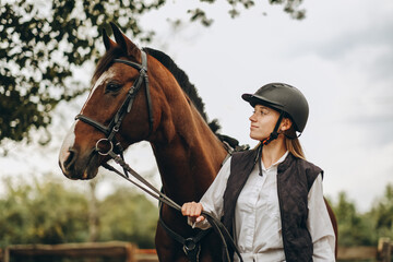 A young female equestrian stands near her horse and prepares for a competition.