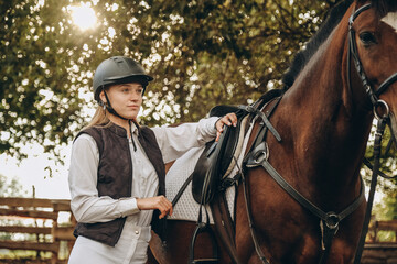 A young female equestrian stands near her horse and prepares for a competition.