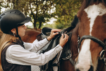 A young woman jockey adjusts the harness on her horse before training.