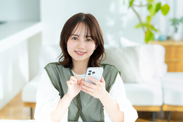 部屋でスマホを操作する若い女性