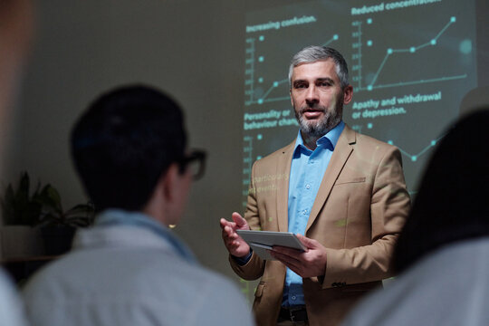 Waist up portrait of mature businessman speaking to audience at medical conference and holding digital tablet while explaining statistics data copy space - Powered by Adobe