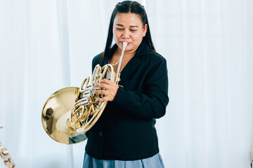 Standing gracefully in a cozy living room, a female musician plays a shiny gold horn. The soft...