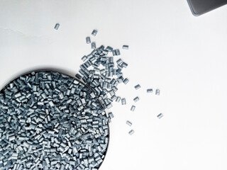 Silver masterbatch plastic granules, polymer carries pigment in a glass cup poured with a white...