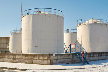 White storage fuel tanks in oil industrial refinery plant area against blue clear sky background, low angle view with copy space