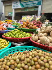Colorful fruits and root vegetables are displayed in woven baskets at an outdoor market. Baskets are red, green, and turquoise.
