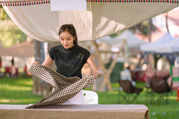 Young asian entrepreneur preparing her market stall by carefully arranging a checkered tablecloth,...