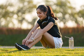 Happy sporty young asian woman tying shoelaces on running shoes, preparing for workout in park at...