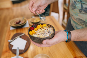 Close up of unrecognizable chef adding seeds with a small spoon to healthy breakfast bowl made with...