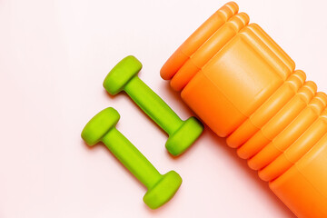 A vibrant flat lay showcasing a pair of lime green dumbbells and an orange foam roller against a soft pink background. Perfect for fitness, wellness