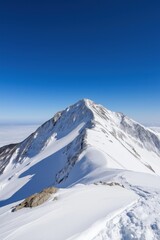 A snow-covered mountain peak with a clear blue sky above it. The mountain is covered in a thick layer of snow, and the sky is a bright, clear blue. The scene is peaceful and serene