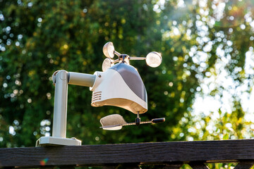 Personal weather station with a black wind vane is mounted on a pole in a garden. Meteorology and...