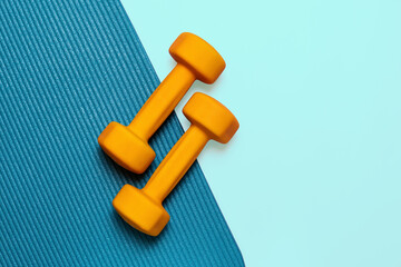 Pair of vibrant yellow dumbbells rests on a textured teal yoga mat, creating a visually appealing image perfect for fitness or wellness projects