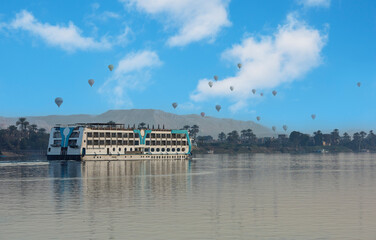 Panoramic landscape view across nile river to luxor west bank with cruise ship mountains and hot air balloons flying in sky