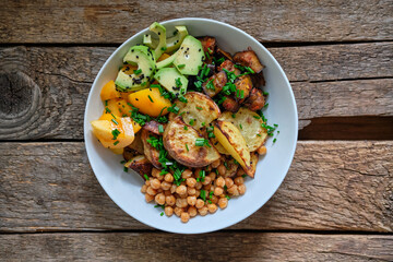 Bowl with fried potatoes, fried eggplant cubes, yellow tomatoes, avocado and crispy chickpeas