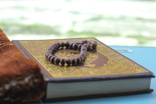 Al Qur'an, Arabic holy book and wooden prayer beads on the table, bokeh background