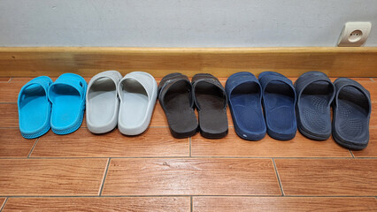 Several pairs of plastic house slippers stand on the ceramic tile floor waiting for guests. Background. Texture. Detail.