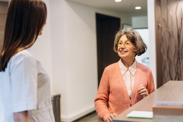 Senior woman talking with receptionist in medical clinic