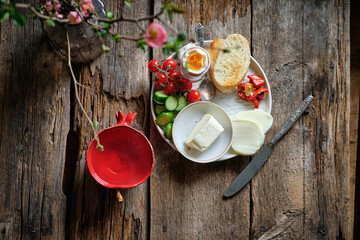 Bowl with boiled egg, cherry tomatoes, toast, butter, cheese, cucumber and hot pepper.
