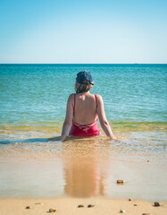 Young woman sits at the water's edge, enjoying the calm sea and sunny weather.