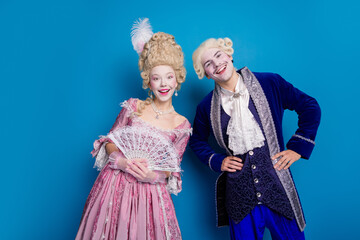 Young couple dressed in exquisite baroque costumes poses against a striking blue background,...