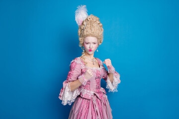 Elegant woman posing in an elaborate corset and vintage dress against a vibrant blue background