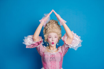 A whimsical woman in an exquisite baroque style dress strikes a playful pose against a vibrant blue backdrop