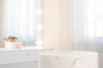 White marble pedestal of cylinder shape for cosmetic product display on blurred dressing room interior background