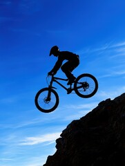Obraz premium Mountain biker in mid-air jump rocky cliff action shot outdoor side view thrilling sports adventure