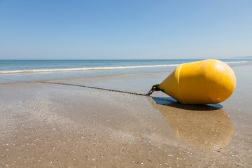 Large yellow buoy lying on the beach of Deauville at ebb tide