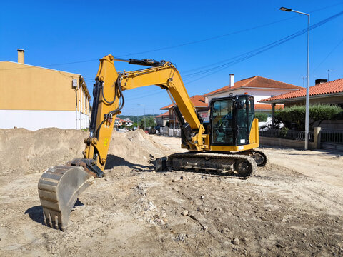 Retroescavadora de esteiras a fazer valas no solo para colocar o saneamento p&uacute;blico em meio a um bairro residencial