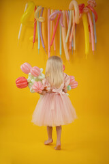 An unrecognizable girl in a pink dress with balloons in the form of tulips on a yellow background.