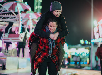 A group of young friends having a great time at a fairground, illuminated by colorful lights during the night, with a joyful atmosphere and warm companionship creating cheerful memories together.