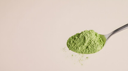 A macro shot of a spoon scooping up bright green matcha powder, the fine particles clinging to its edges. The background is a soft neutral beige, enhancing the visual impact of the green hue. The