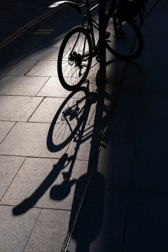 Morning sunlight creating strong bicycle shadows on a London sidewalk.