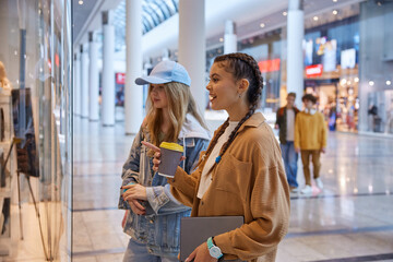 Teenage girls friends looking through showcase window in shopping mall