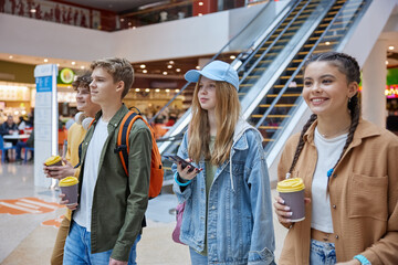 Teenagers friends smiling and talking while walking through shopping mall hall