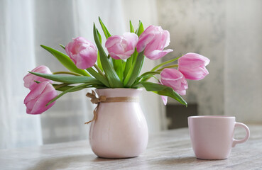 Obraz premium Fresh pink tulip flowers bouquet and pink cup of coffee. On white wooden table. White spring interior