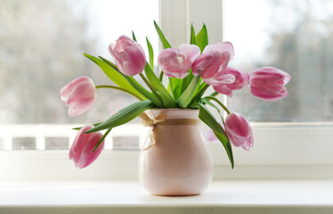 Delicate pink tulip flowers in a pink vase on the window in the spring morning.