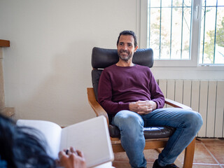 Relaxed male patient smiling at a therapy session with a female psychologist. The setting is warm...