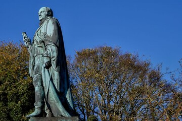 Bronze statue with autumn trees and blue sky.