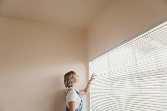 Young woman looking through blinds at the window