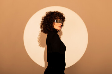 Woman wearing futuristic glasses and standing against beige background