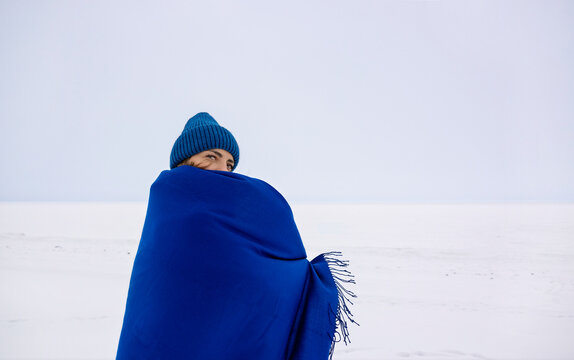 Woman wrapped in a blue blanket standing in a snowy field during winter