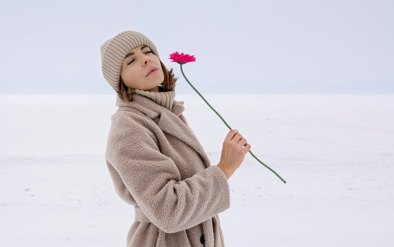 Woman in winter clothing holding a red flower in a snowy field