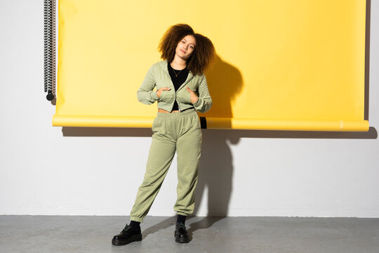 Young woman with curly hair standing against wall with yellow backdrop