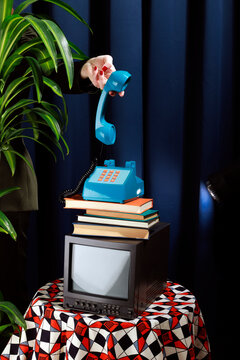 Vintage elegant office studio shoot with a hand holding a telephone receiver over a stack of books and a television