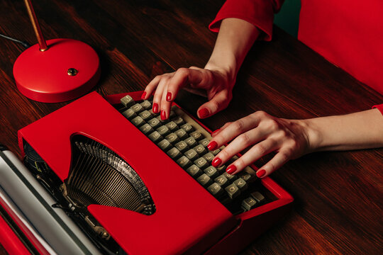 Woman in red dress typing on a vintage typewriter at a wooden table in an office setting