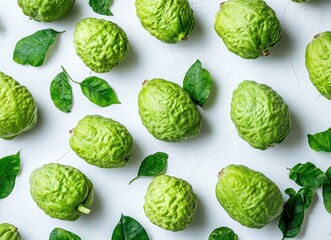 Fototapeta premium Fresh Green Citrus Fruits with Gritty Texture Surrounded by Vibrant Green Leaves on a Light Surface for Use in Food and Nature Themes