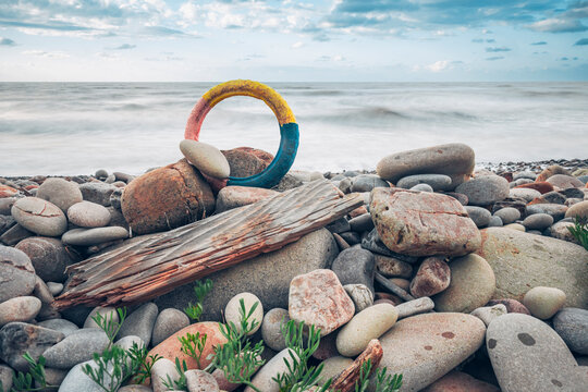Colorful rubber wheel among pebbles and driftwood on a polluted beach