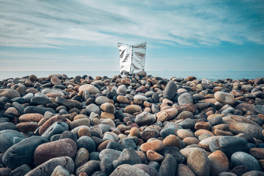 Silver chip bag among pebbles on a polluted beach